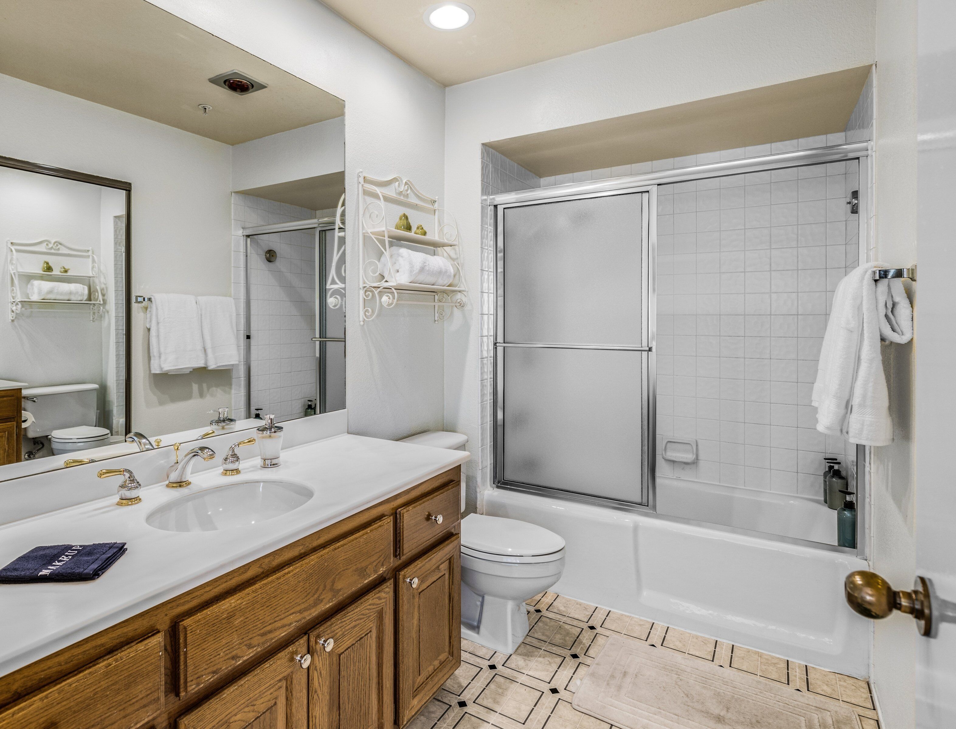 A bathroom with a large mirror, two sinks, a toilet, and a walk-in shower.