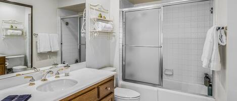 A bathroom with a large mirror, two sinks, a toilet, and a walk-in shower.