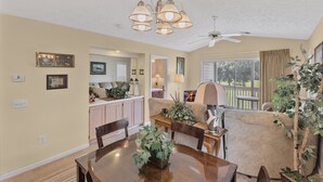 A dining area with a round table, chairs, and a chandelier. There is a kitchen in the background with cabinets and a countertop. - River Oaks 2I (Myrtle Beach)