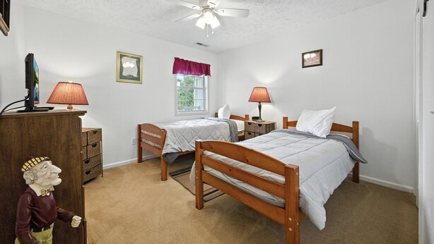 A bedroom with two single beds, a ceiling fan, a window with a red valance, and a wooden dresser. - River Oaks 2I (Myrtle Beach)
