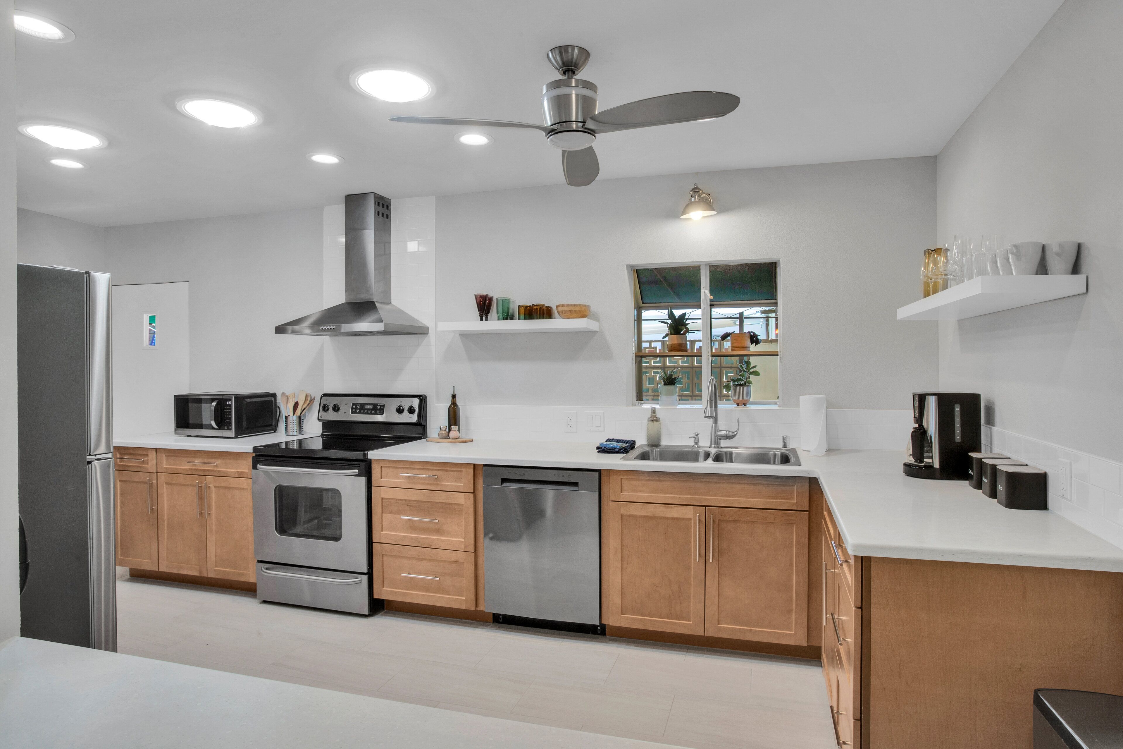 A modern kitchen with stainless steel appliances, wooden cabinets, and a ceiling fan.