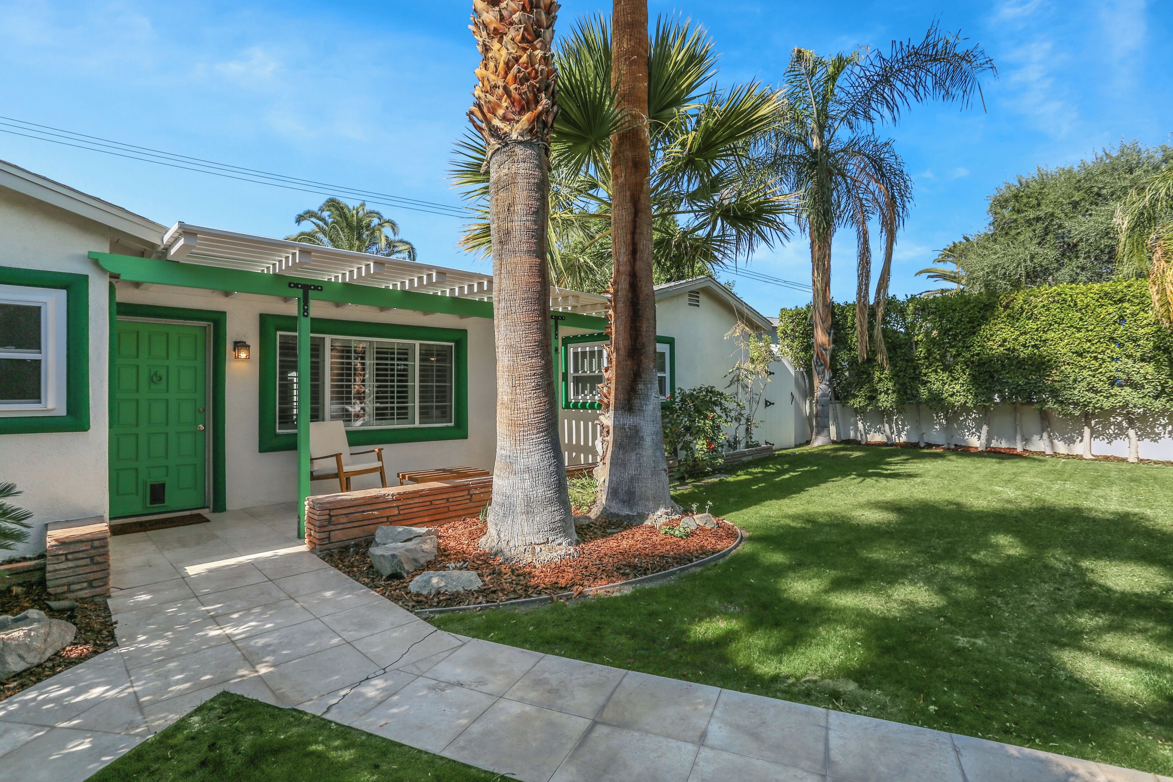 A house with a green door, a brick bench, and a well-maintained lawn with palm trees.