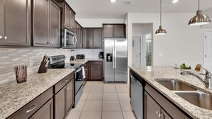 A modern kitchen with dark cabinets, stainless steel appliances, granite countertops, and pendant lighting. - Smm1811 (Davenport)
