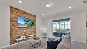 A living room with a wooden wall, a TV, a sofa, a coffee table, and a window with a view. - Smm1811 (Davenport)