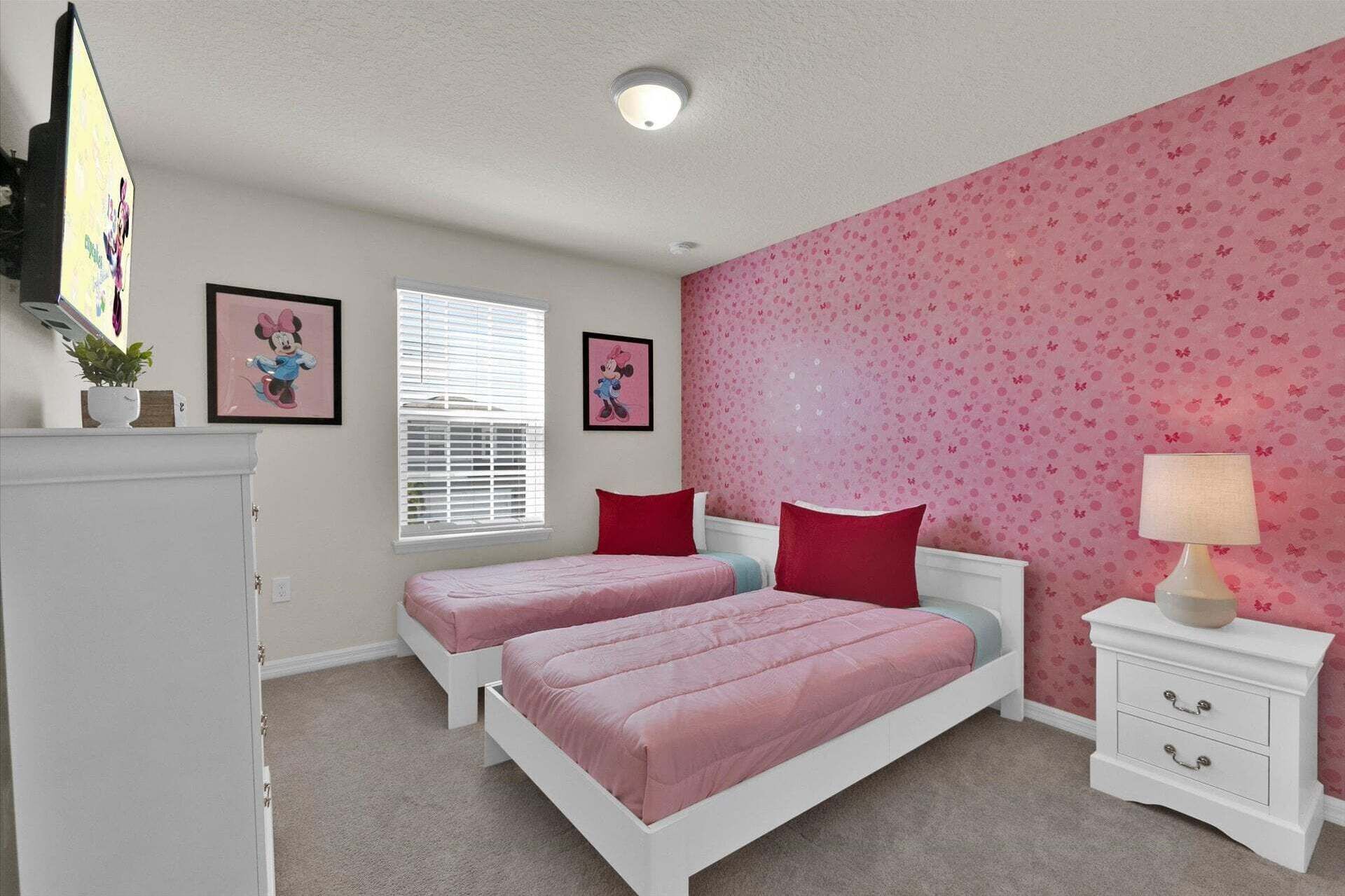 A bedroom with two beds, a dresser, a lamp, and a window with blinds.