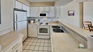 A compact kitchen with white cabinets, a microwave, a stove, and a sink. - Sands Beach Club 123 (Myrtle Beach)