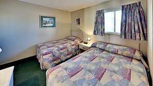 A hotel room with two beds, a nightstand, a lamp, a window with curtains, and two framed pictures on the wall. - Sands Beach Club 123 (Myrtle Beach)
