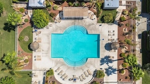 Vista aérea de un complejo turístico con piscina central, zonas de descanso y jardines ajardinados.
