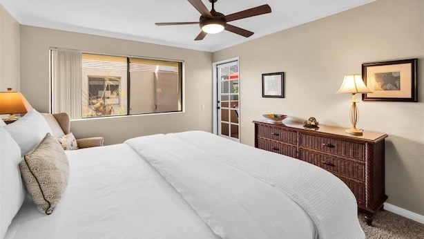 Un dormitorio con cama, ventilador de techo, cómoda, lámpara y ventana con cortinas.