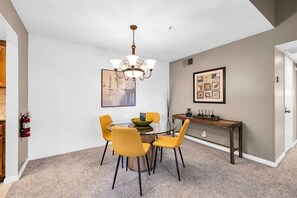 A dining area with a round table, four yellow chairs, a chandelier, and a fire extinguisher on the wall. - Plaza Villas 571 (Palm Springs)