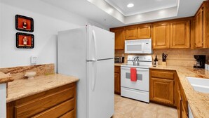 Una cocina moderna con electrodomésticos blancos, gabinetes de madera y encimeras de granito.