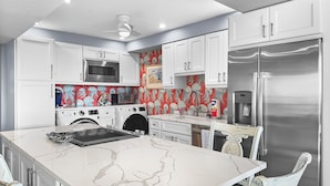 A modern kitchen with white cabinetry, a stainless steel refrigerator, a microwave, a toaster, and a washing machine. - Sandy Cove (Siesta Key)