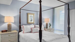 A four-poster bed with white bedding and red trim, flanked by two nightstands with lamps and a framed picture above. - Sandy Cove (Siesta Key)
