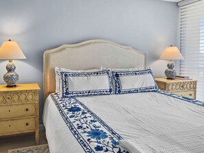 A neatly made bed with white bedding and blue floral patterns, flanked by two bedside tables with lamps and decorative vases. - Sandy Cove (Siesta Key)