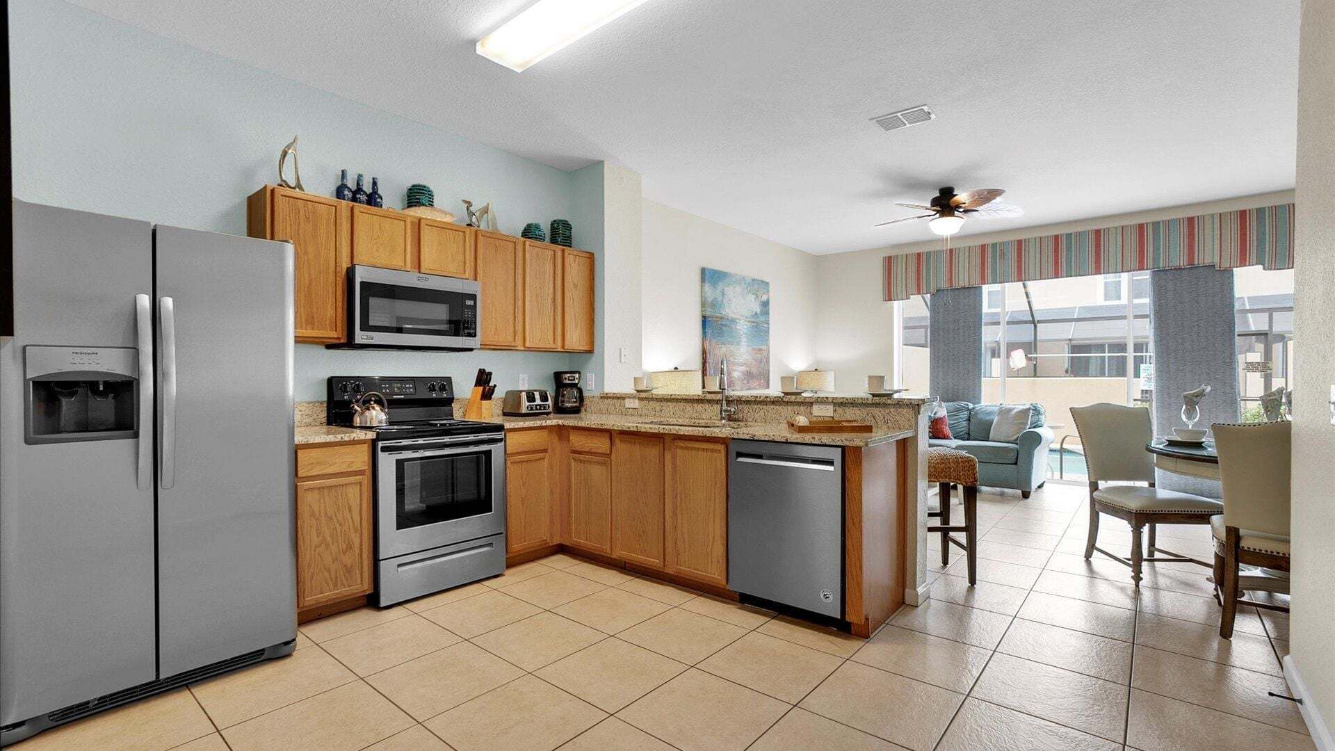 A modern kitchen with a refrigerator, stove, microwave, and dishwasher. There is a dining area with a table and chairs, and a view of the outside.