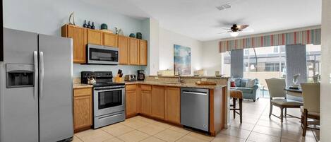 A modern kitchen with a refrigerator, stove, microwave, and dishwasher. There is a dining area with a table and chairs, and a view of the outside.