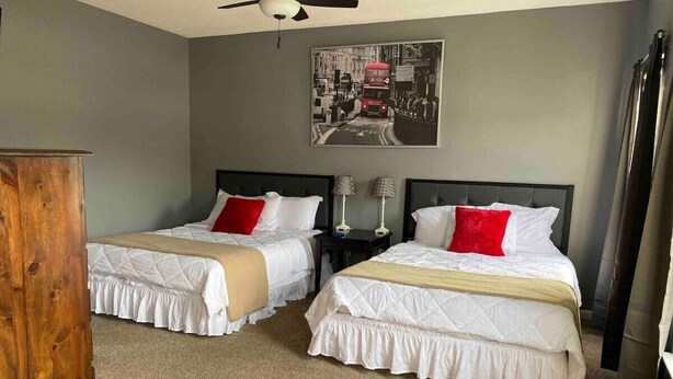 A hotel room with two beds, a ceiling fan, a wooden cabinet, and a cityscape painting on the wall. - Putters Hideaway @ Legends Golf Resort (Myrtle Beach)