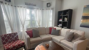 A living room with a sectional sofa, a patterned armchair, a wooden coffee table, a ceiling fan, a bookshelf, and a painting on the wall. - Putters Hideaway @ Legends Golf Resort (Myrtle Beach)