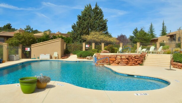 A swimming pool with a stone wall and lounge chairs, surrounded by greenery and residential buildings. - Santa Susana (Sedona)