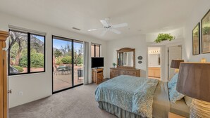 A bedroom with a large sliding glass door leading to a patio, a ceiling fan, a bed with a patterned bedspread, a dresser, and a television. - Santa Susana (Sedona)