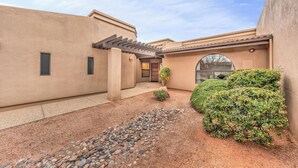 A building with a beige exterior, a covered patio area, and a small garden with rocks and shrubs. - Santa Susana (Sedona)
