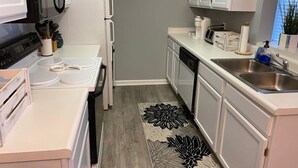A compact kitchen with white cabinets, a microwave, stove, and a sink.
