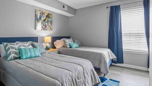 A bedroom with two beds, a ceiling fan, a window with curtains, and a painting on the wall.