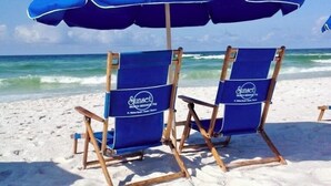 Zwei Liegen mit einem blauen Sonnenschirm an einem Sandstrand.