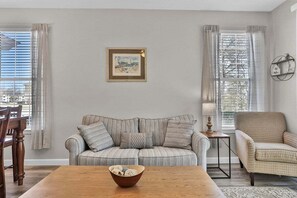 A living room with a striped sofa, a wooden coffee table, and a framed picture on the wall. - River Oaks 57B (Myrtle Beach)