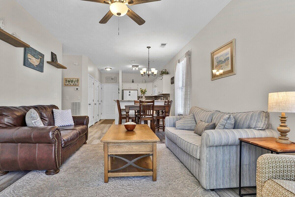 A living room with a brown leather sofa, a striped sofa, a wooden coffee table, and a dining area with a chandelier.
