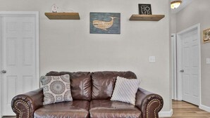 Ein braunes Ledersofa mit dekorativen Kissen, eine an der Wand befestigte Holzablage mit einer Walillustration und ein Schild mit der Aufschrift 'Welcome'.