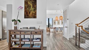A modern kitchen with wooden flooring, a wooden console table with books, a vase with flowers, and a large abstract painting on the wall. - Shoreline Villa by Rove Rooftop & Beach Access (Hollywood)