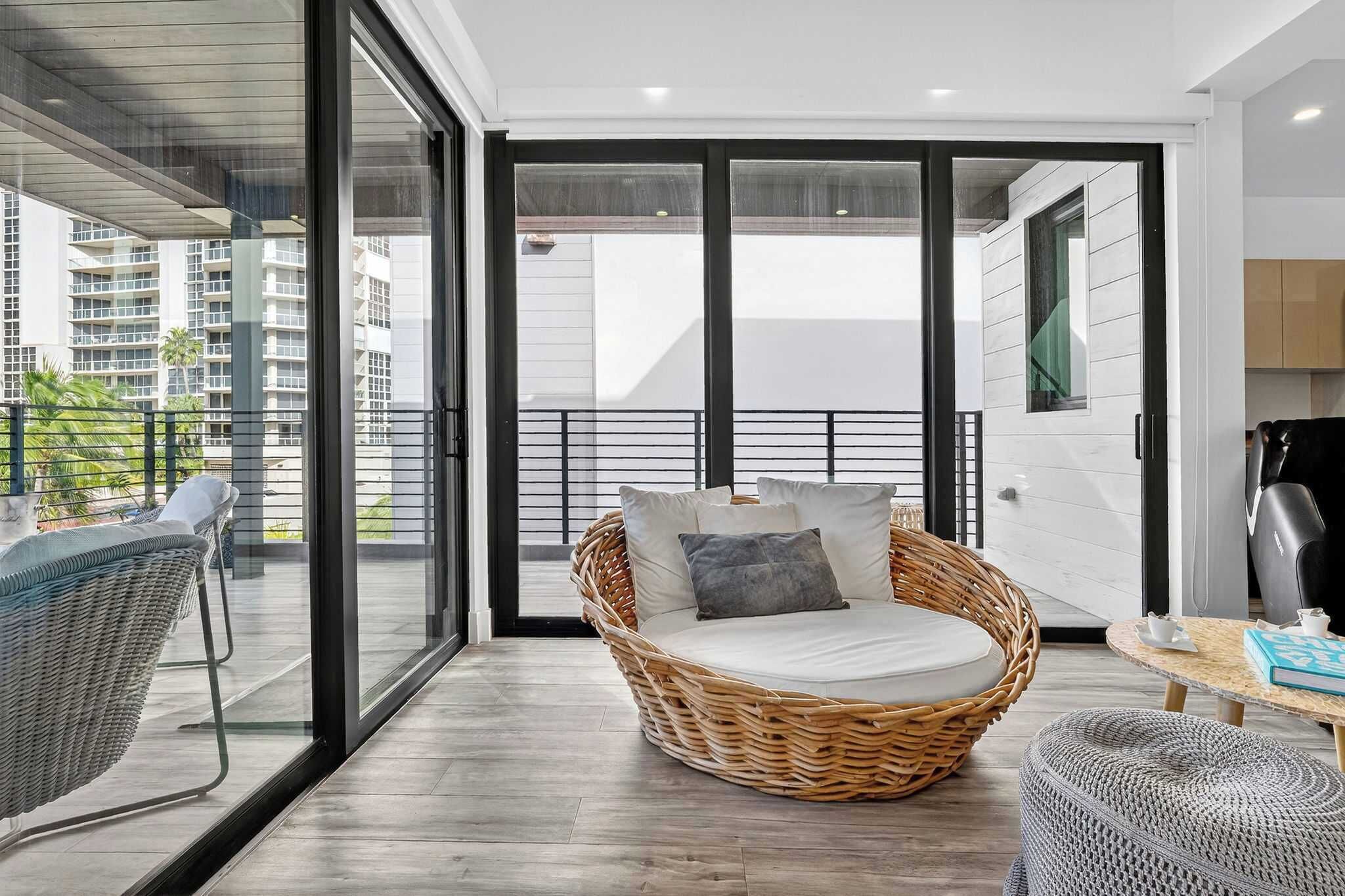 A modern living room with a wicker sofa, a round table, and a glass door leading to a balcony.