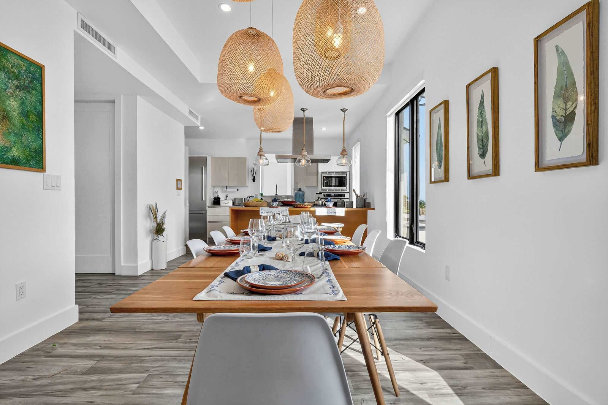 A modern dining area with a wooden table set for six, white walls, and a kitchen in the background.