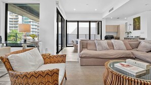 A modern living room with a sofa, chairs, and a coffee table. There is a balcony with a view of buildings. - Shoreline Villa by Rove Rooftop & Beach Access (Hollywood)