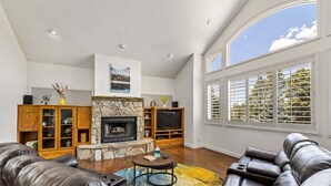 A living room with a stone fireplace, leather sofas, a TV, and a large window with blinds. - Sinagua Heights Flagstaff (Flagstaff)