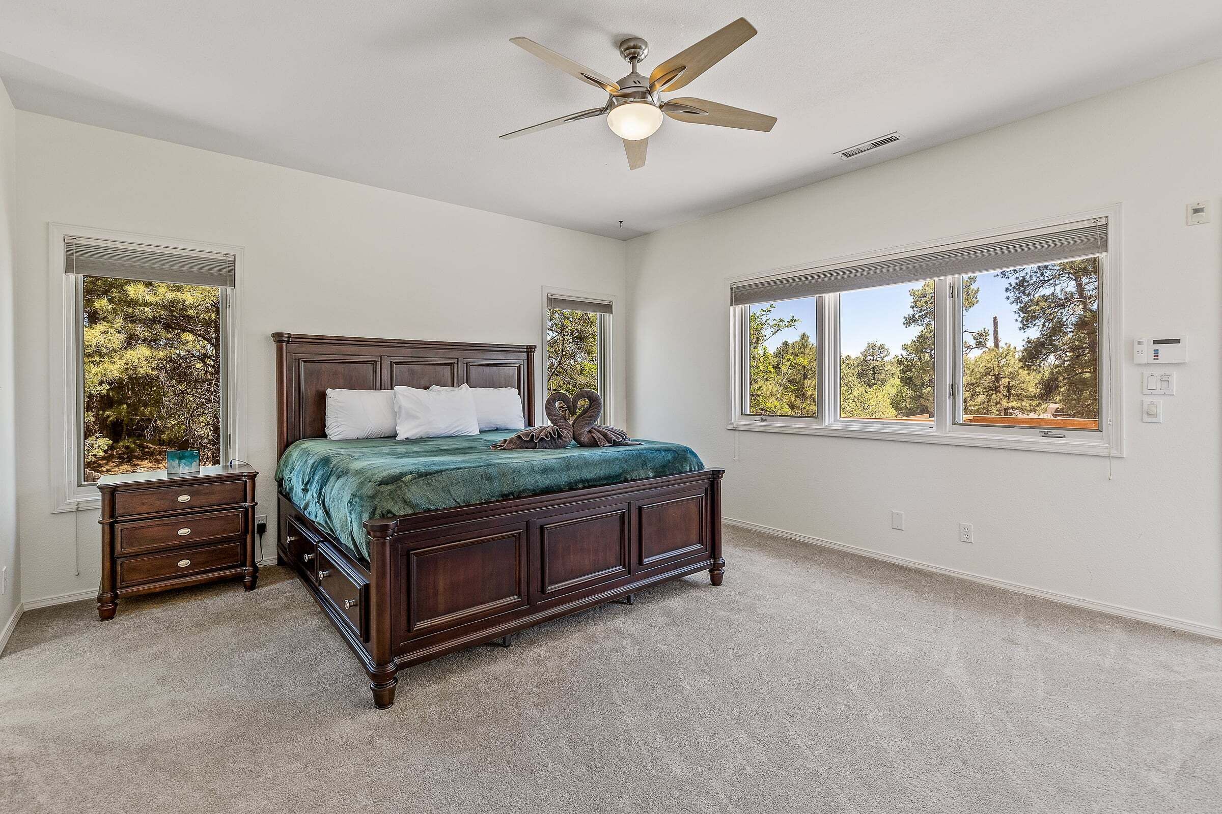A bedroom with a bed, nightstand, dresser, ceiling fan, and large windows.