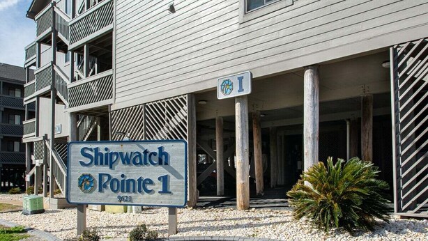 En byggnad med en skylt som visar texten ”Shipwatch Pointe 1” och en parkeringsplats med en palmpalm.