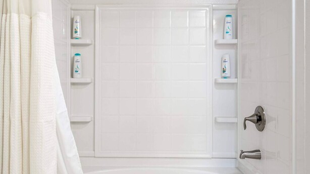Une salle de bain avec une baignoire, des murs recouverts de carreaux blancs et deux étagères contenant des articles de toilette.