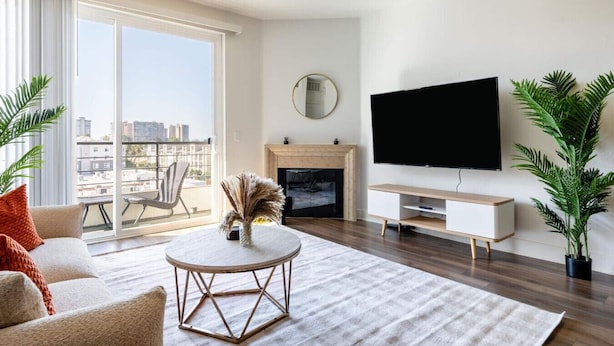 Ein modernes Wohnzimmer mit Kamin, großem Fernseher und Balkon mit Blick auf die Stadt.