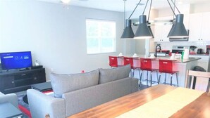 Een moderne woonkamer met een grijze bank, een houten eettafel en een televisie op een zwart dressoir.