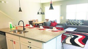 Een keuken met een centraal eiland, een eethoek met een tafel en stoelen, en een woonkamer met een bank en een kamerbreed tapijt.