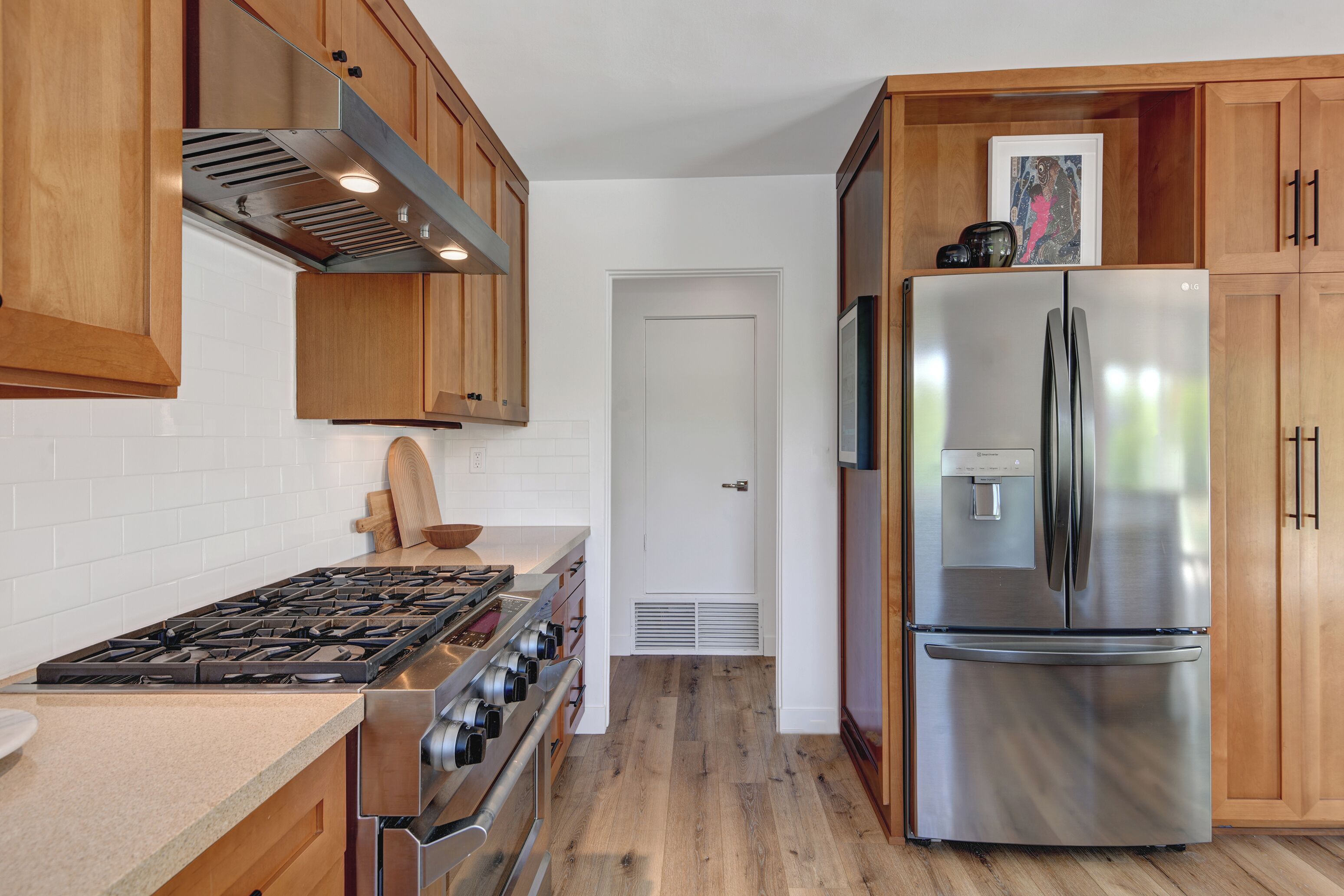 A kitchen with wooden cabinets, a stainless steel refrigerator, a gas stove, and a white door.