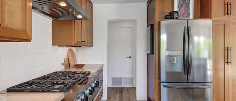 A kitchen with wooden cabinets, a stainless steel refrigerator, a gas stove, and a white door.