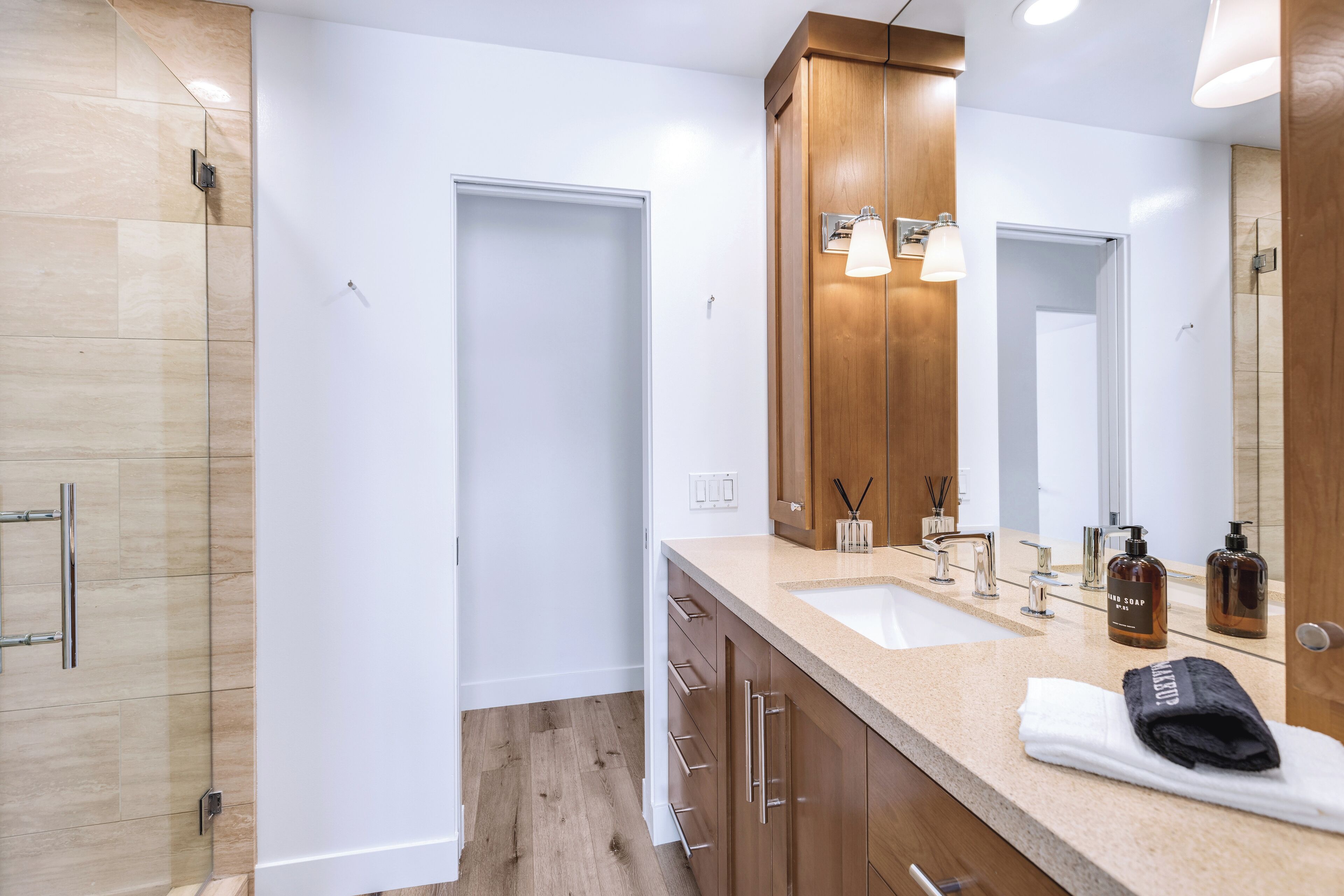 Une salle de bain moderne avec deux vasques, des meubles en bois, une cabine de douche en verre et un grand miroir.