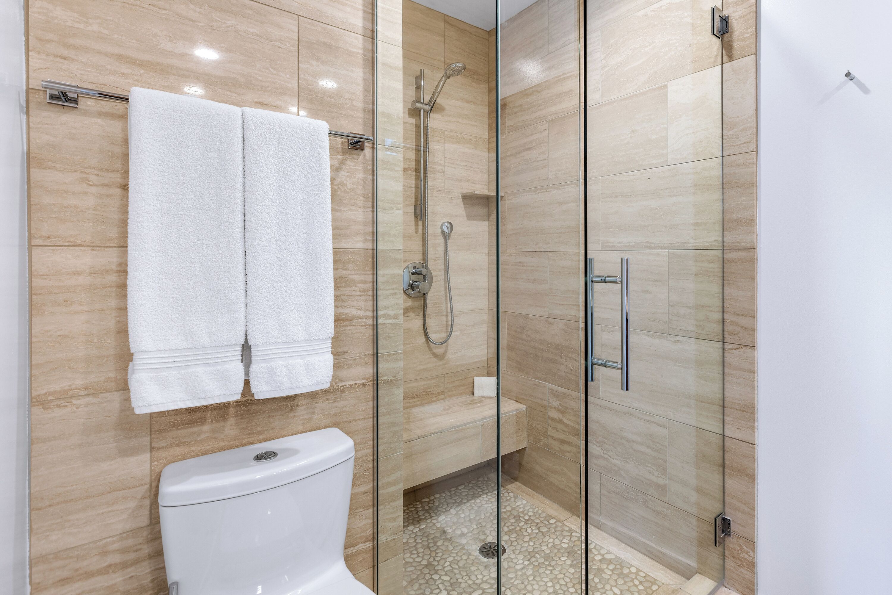 A modern bathroom with a glass-enclosed shower, a toilet, and two white towels hanging on a rack.