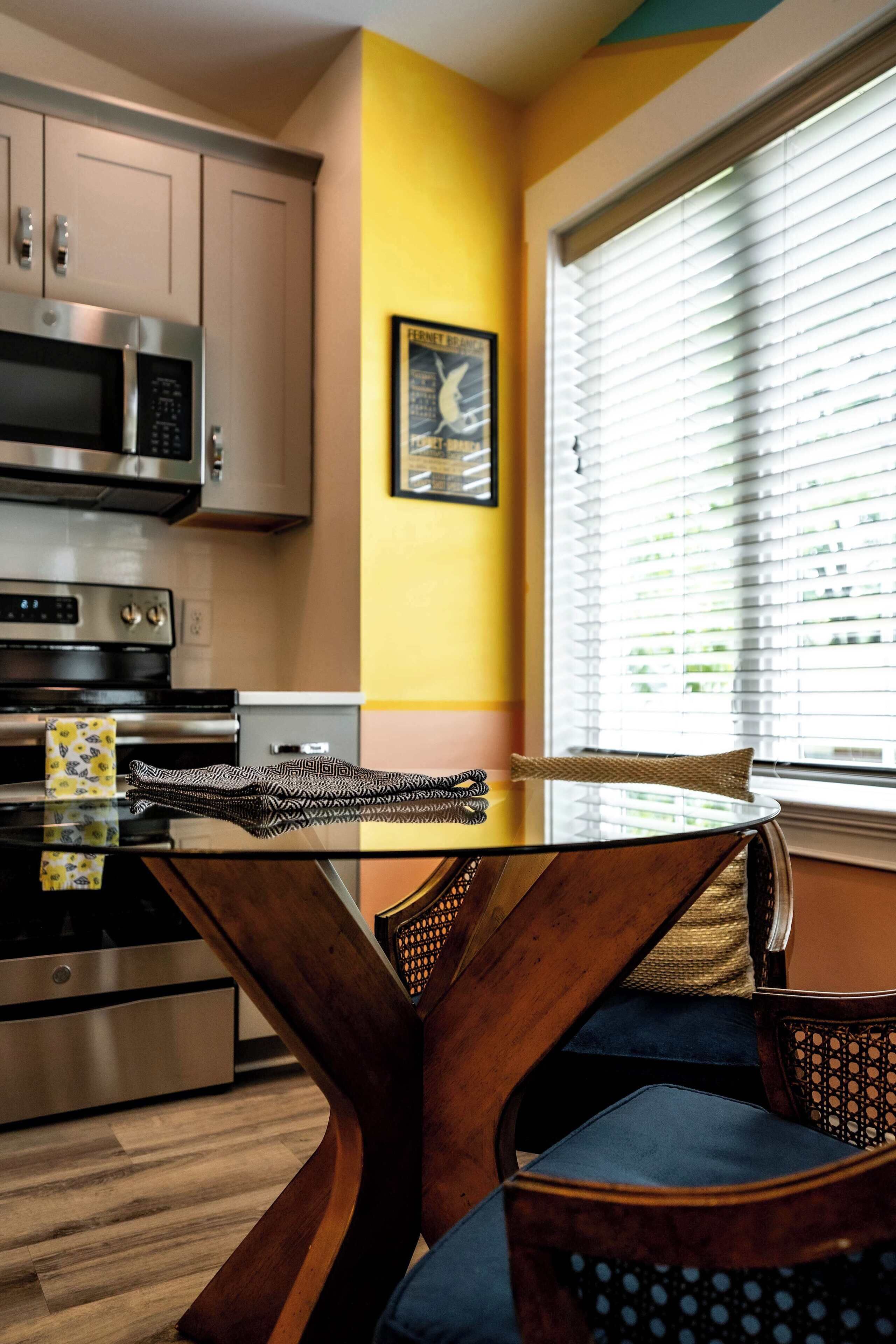 A modern kitchen with stainless steel appliances, a glass dining table, and wooden chairs.