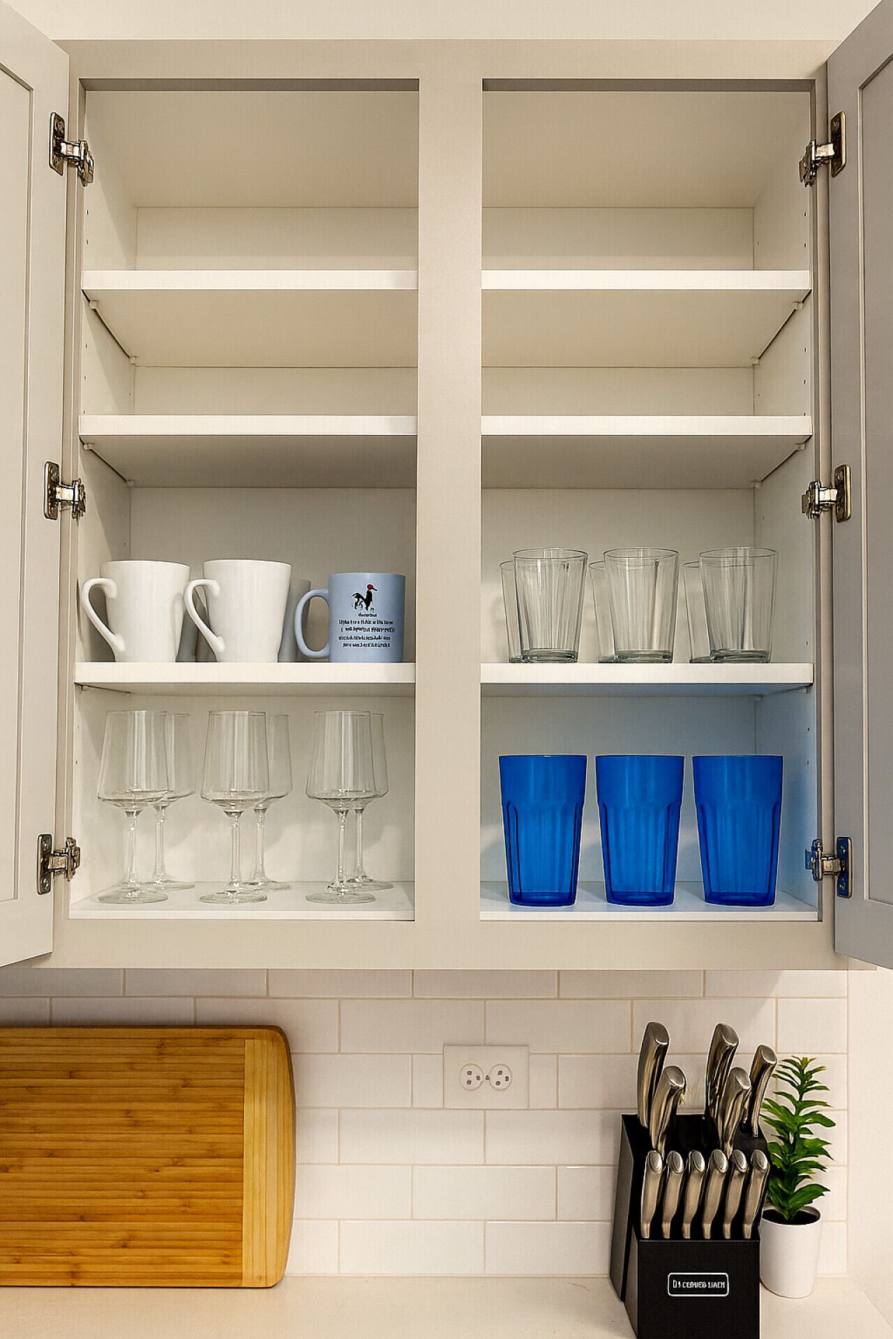 A kitchen with white cabinets, a wooden cutting board, a knife block, and a potted plant.
