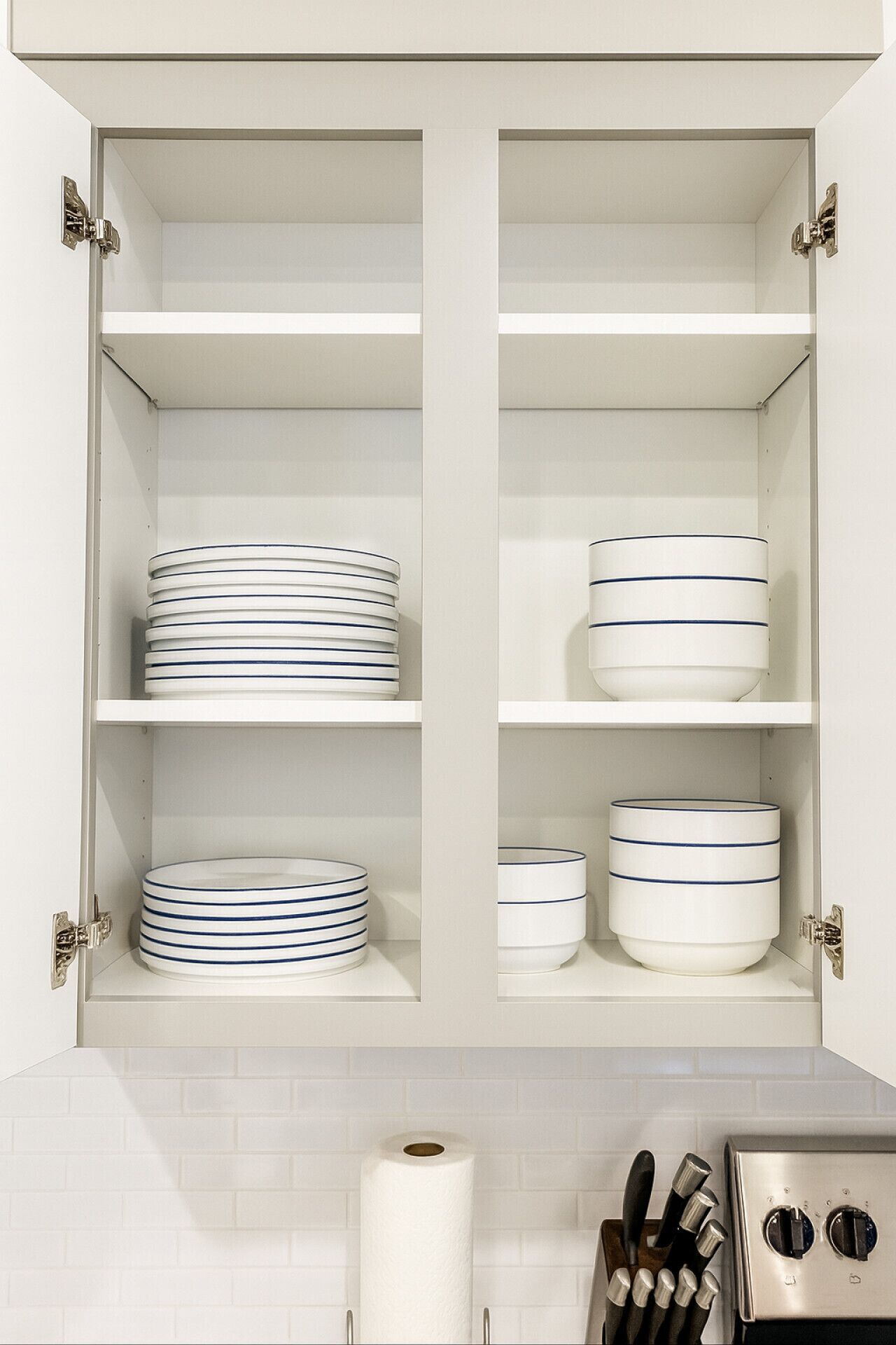 A kitchen cabinet with white interior shelves, holding stacked plates and bowls.