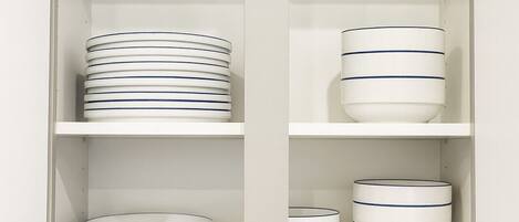 A kitchen cabinet with white interior shelves, holding stacked plates and bowls.